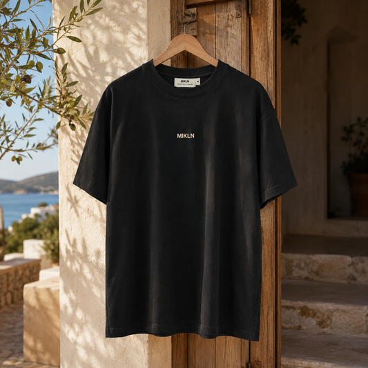 MIKLN Original T-shirt in zwart aan een hanger in een mediterrane setting