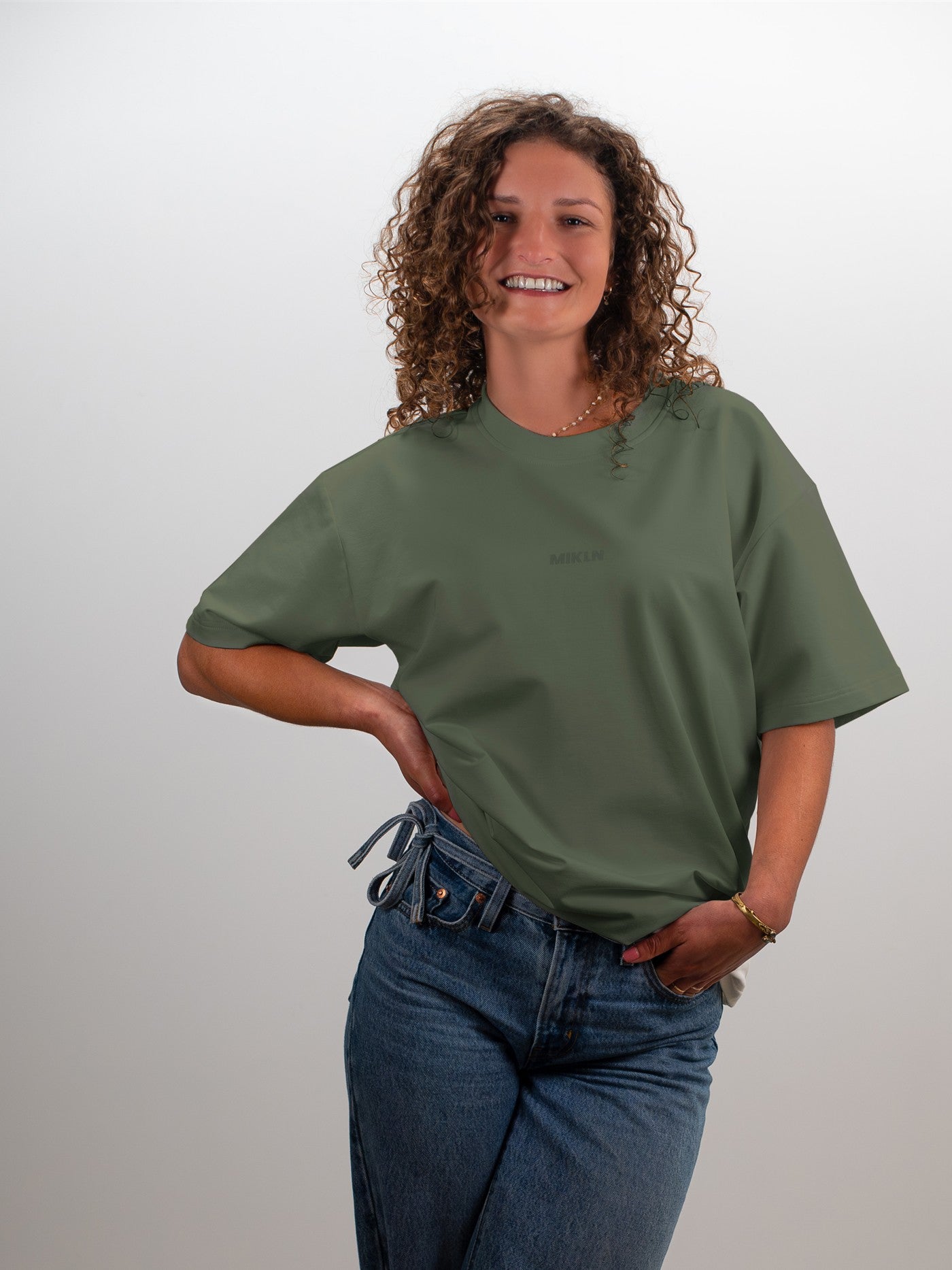 Vrouw draagt het MIKLN T02 T-shirt in groen, oversized fit met ton-sur-ton logo, gecombineerd met wijde jeans