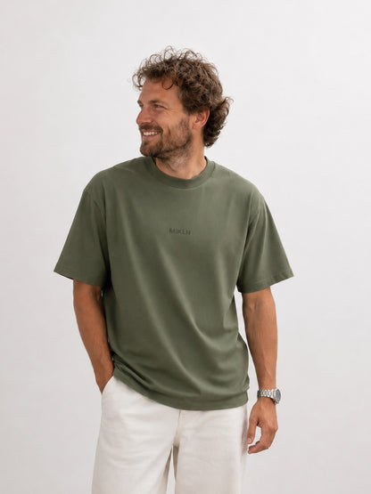 Man draagt het MIKLN T02 T-shirt in groen, oversized fit met ton-sur-ton logo, gecombineerd met witte broek