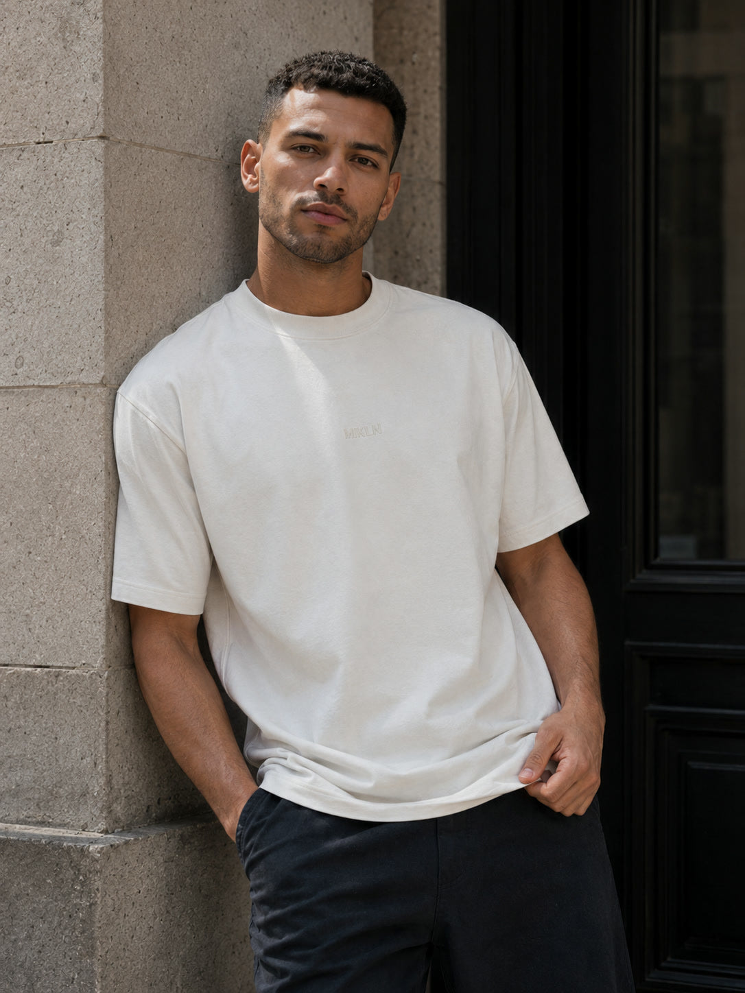 MIKLN T 02 off white T-shirt leunend tegen een muur