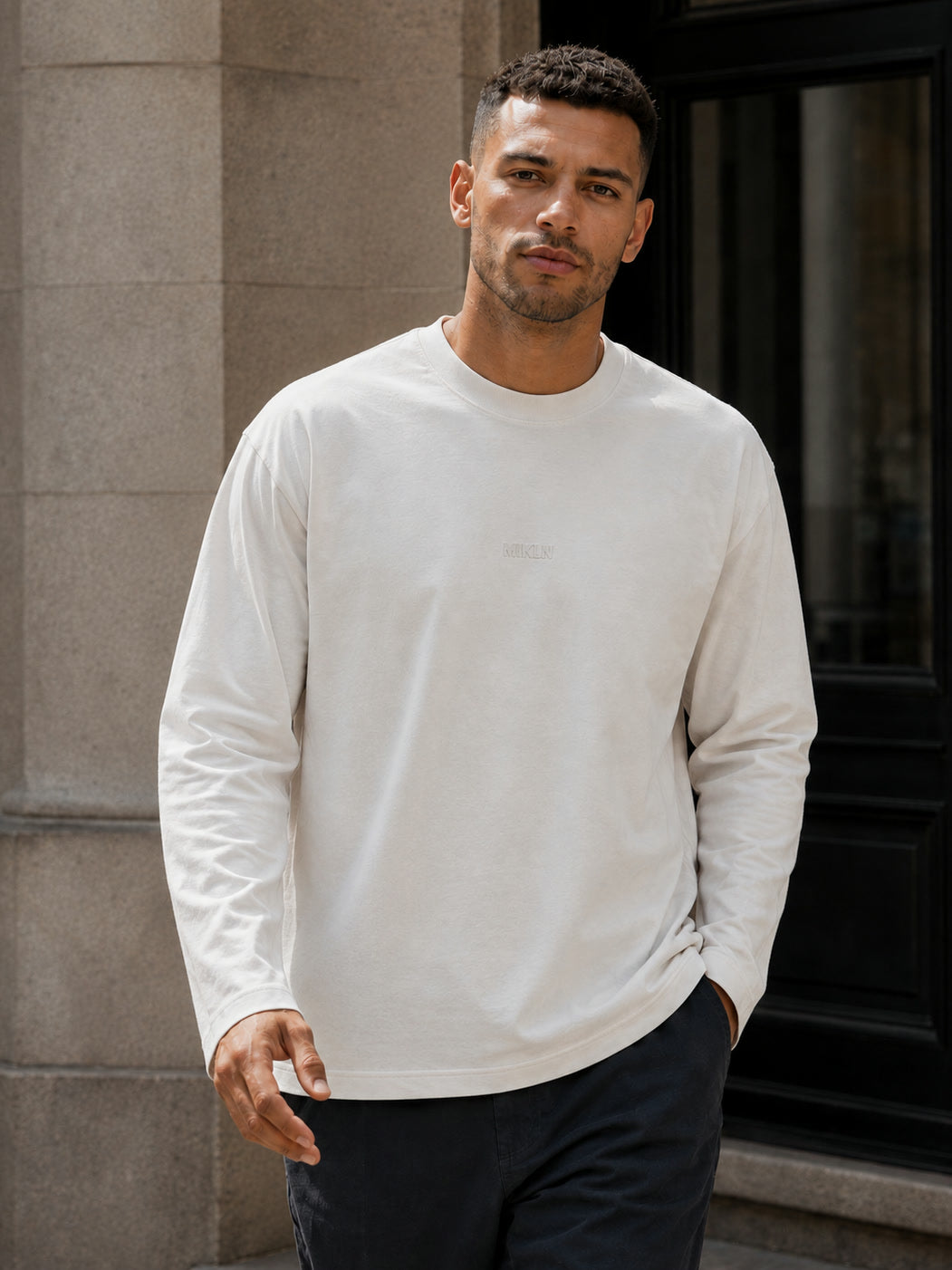 MIKLN T 03 off white long sleeve gedragen tegen een gevel in de stad, relaxed fit